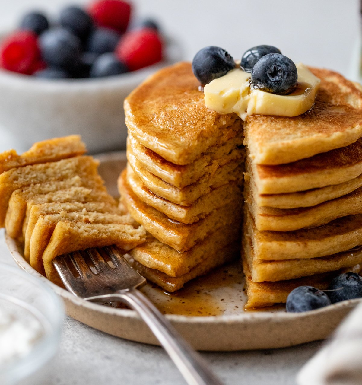 A stack of fluffy cottage cheese pancakes topped with butter and blueberries sits on a plate, with syrup drizzling down