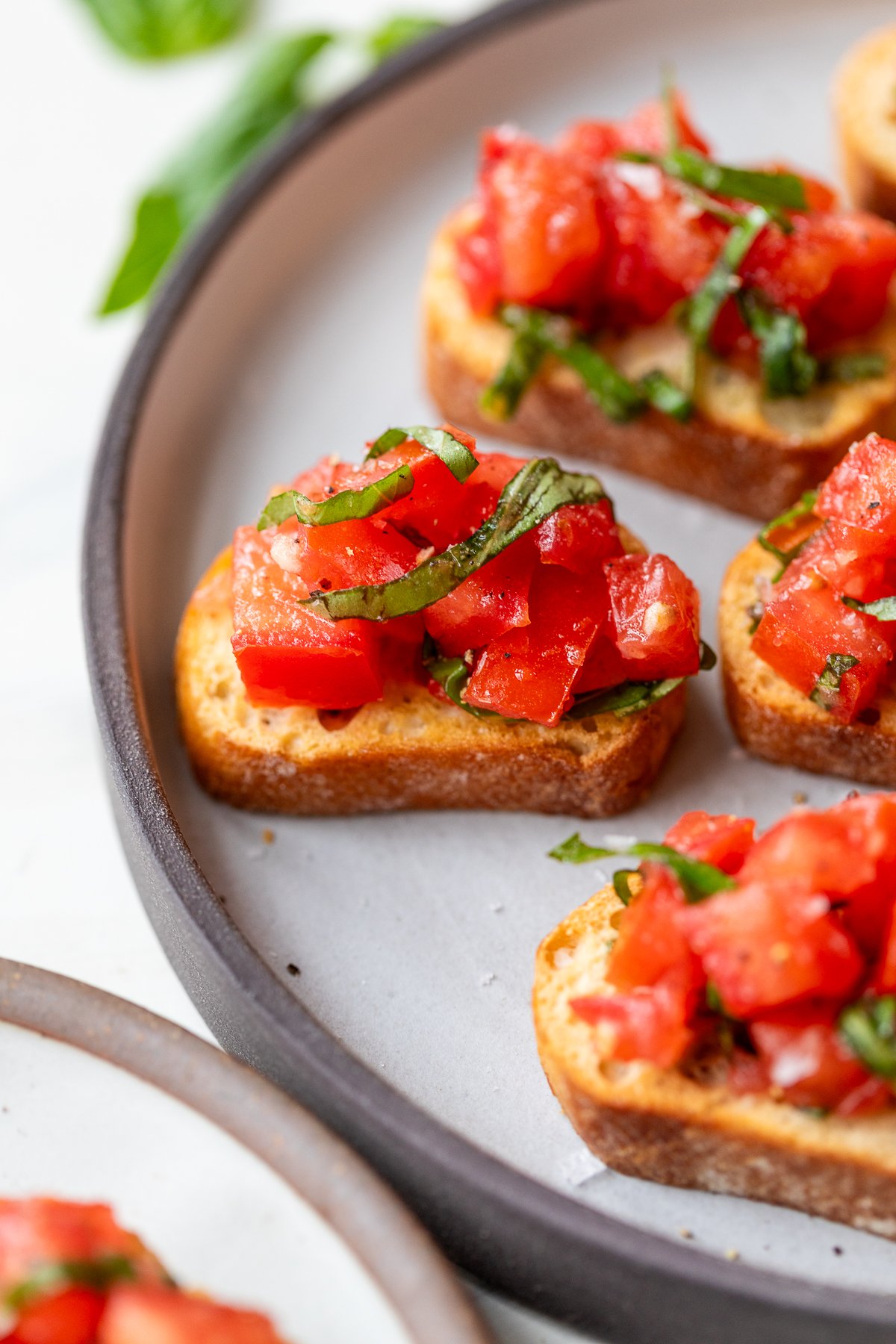 Several pieces of toasted bread topped with chopped tomatoes and fresh basil are arranged on a round plate, creating a colorful bruschetta appetizer.