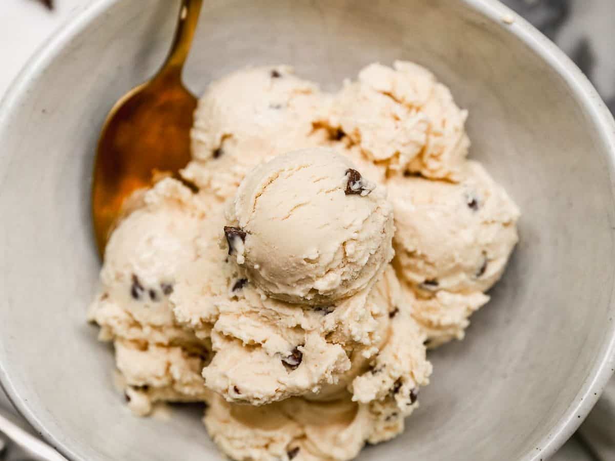 A bowl of creamy cottage cheese ice cream with chocolate chips, served with a gold spoon on a marble surface.