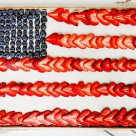 Rectangular sheet cake dessert decorated like an American flag with blueberries and rows of sliced strawberries on white frosting.
