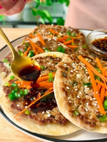 A hand drizzles dark soy sauce over crispy smashed dumpling tacos