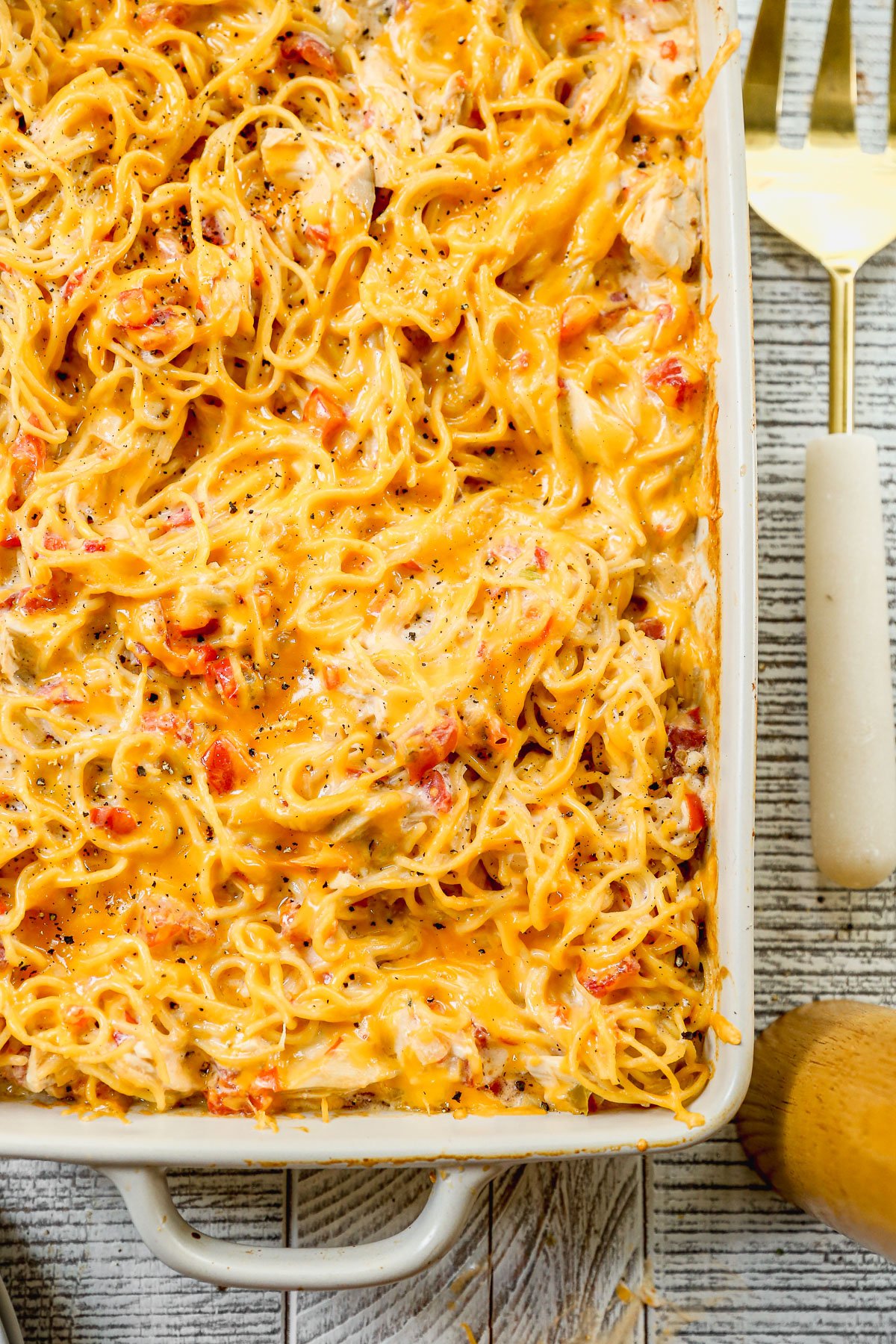 Baked cheesy chicken spaghetti casserole with shredded chicken and peppers in a white dish, topped with melted cheese and black pepper.
