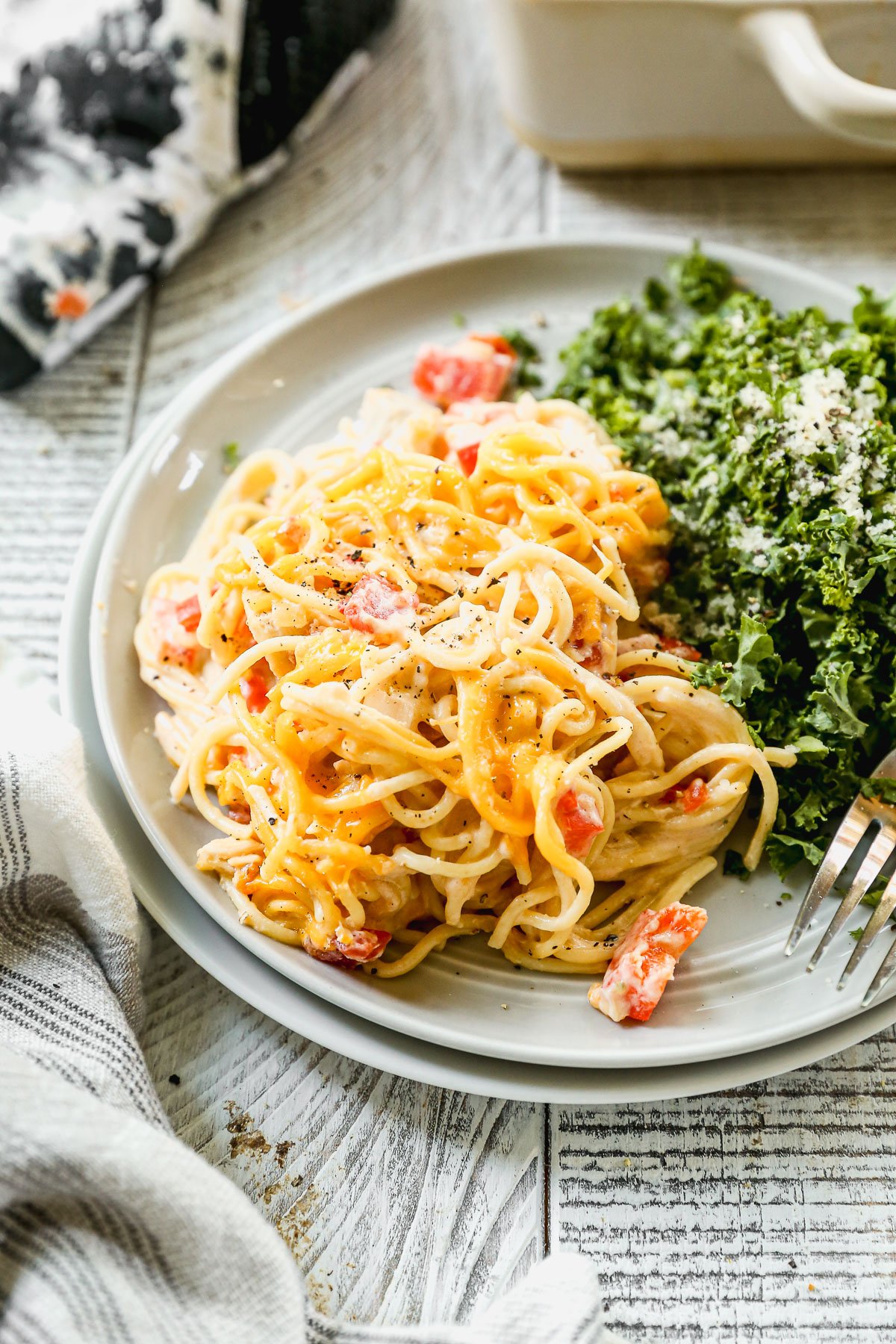 Plate of creamy chicken spaghetti with diced red bell peppers, served with a side of leafy green salad and a fork.