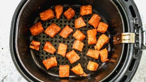 Chunks of seasoned salmon arranged inside an air fryer basket, ready to be cooked.