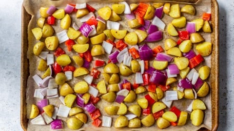 Chopped potatoes, red bell peppers, and red onions on a parchment-lined baking sheet, ready to roast.