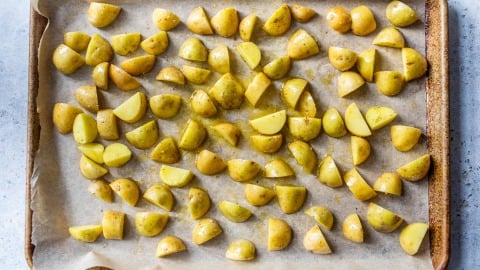 Quartered baby potatoes tossed in oil and spices, spread on a parchment-lined baking sheet, ready for roasting.