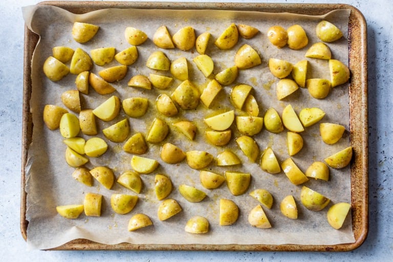 Quartered baby potatoes tossed in oil and spices, spread on a parchment-lined baking sheet, ready for roasting.