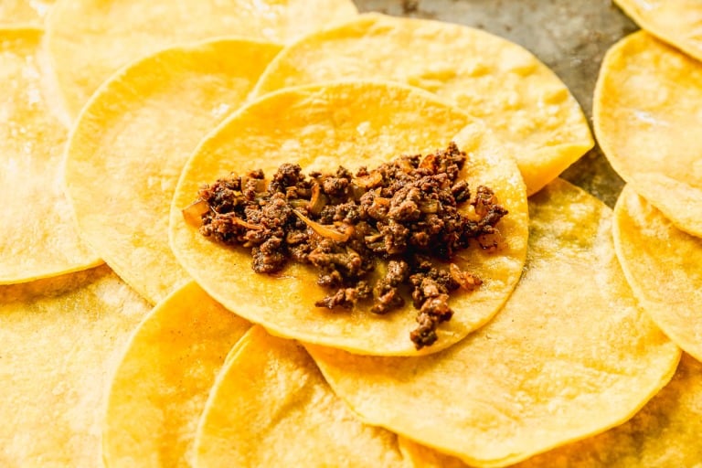 Corn tortillas with seasoned ground beef filling are arranged on a surface, ready to be folded for enchiladas.