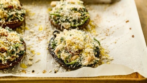 Stuffed portobello mushrooms topped with breadcrumbs and greens on a parchment-lined baking sheet.