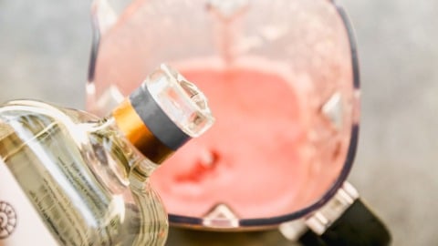 A bottle pouring tequila into a blender filled with a watermelon juice.