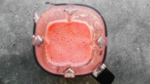 Blender filled with frothy blended watermelon, viewed from above on a gray countertop.