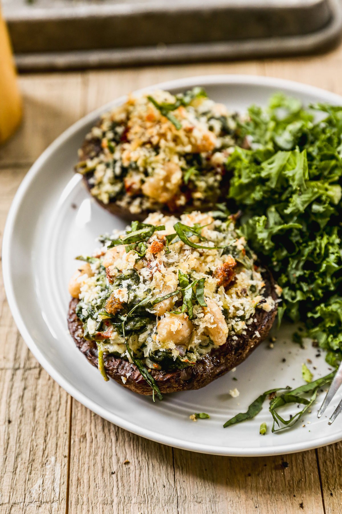 Stuffed portobello mushrooms topped with breadcrumbs and herbs, served with a side of fresh kale on a white plate.