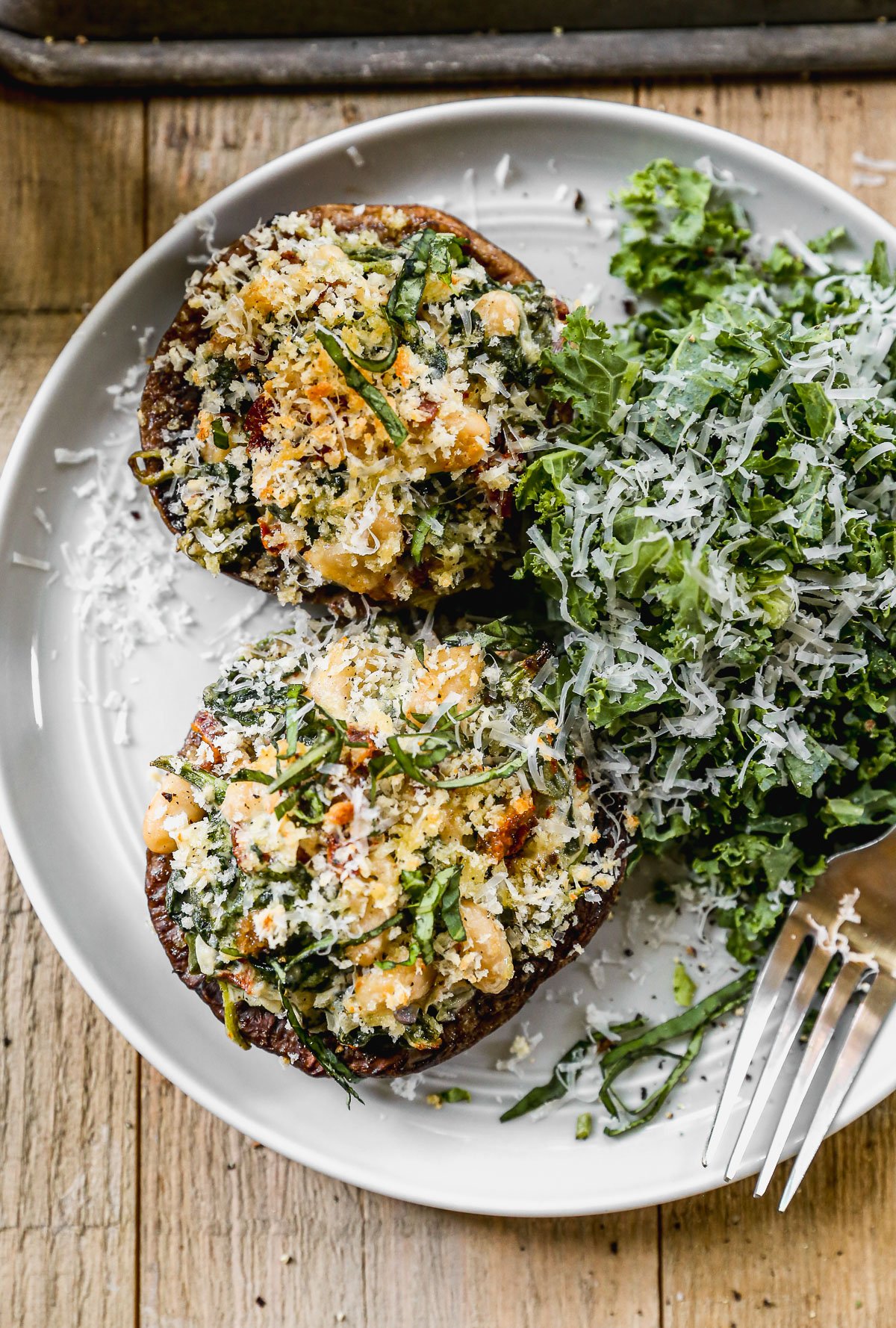 Two stuffed portobello mushrooms topped with greens and cheese, served with a side of leafy salad on a white plate.