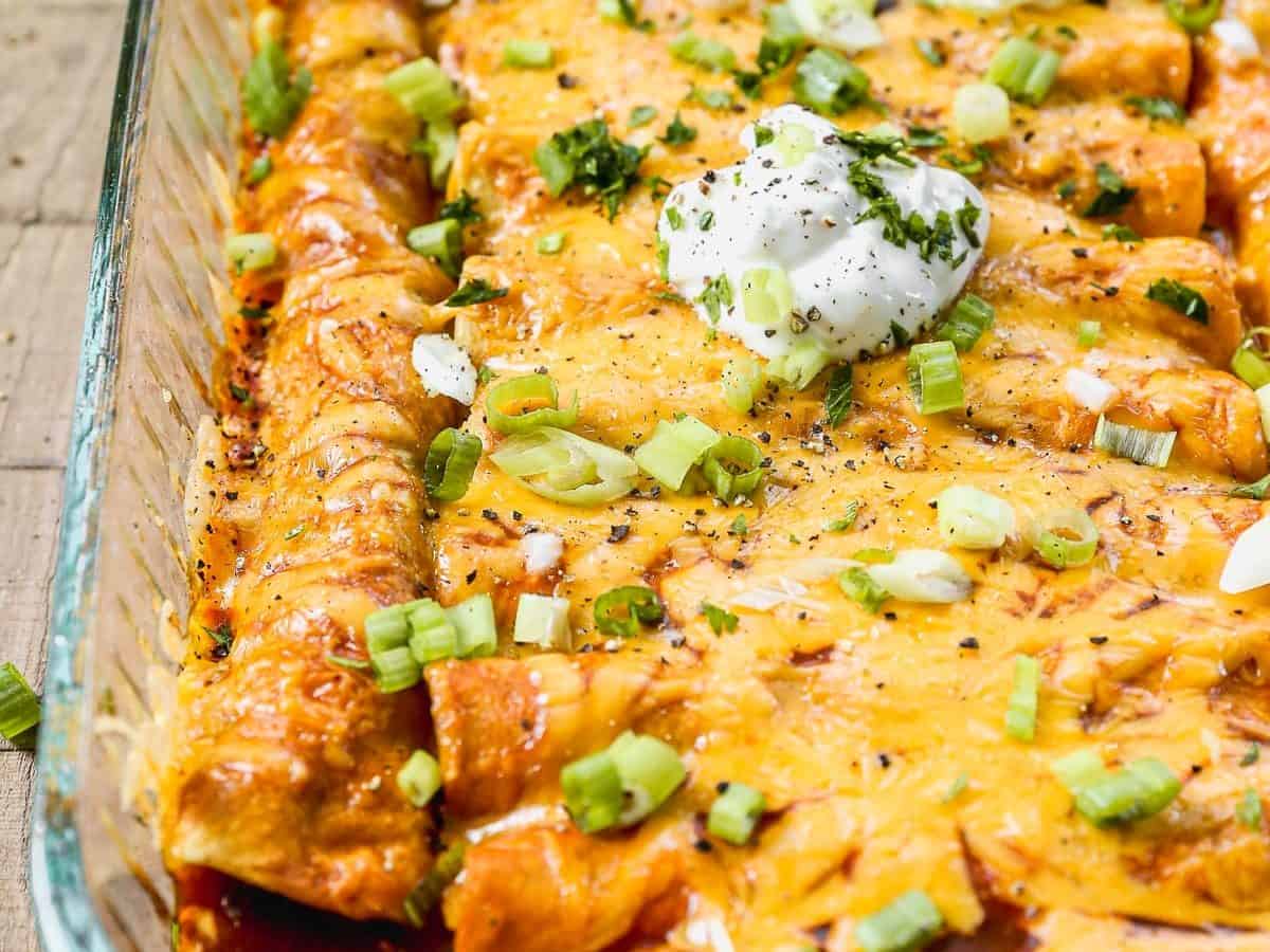 Cheesy ground beef enchiladas topped with sour cream, chopped green onions, and herbs in a glass baking dish.