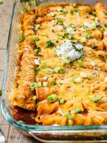 Cheesy ground beef enchiladas topped with sour cream, chopped green onions, and herbs in a glass baking dish.