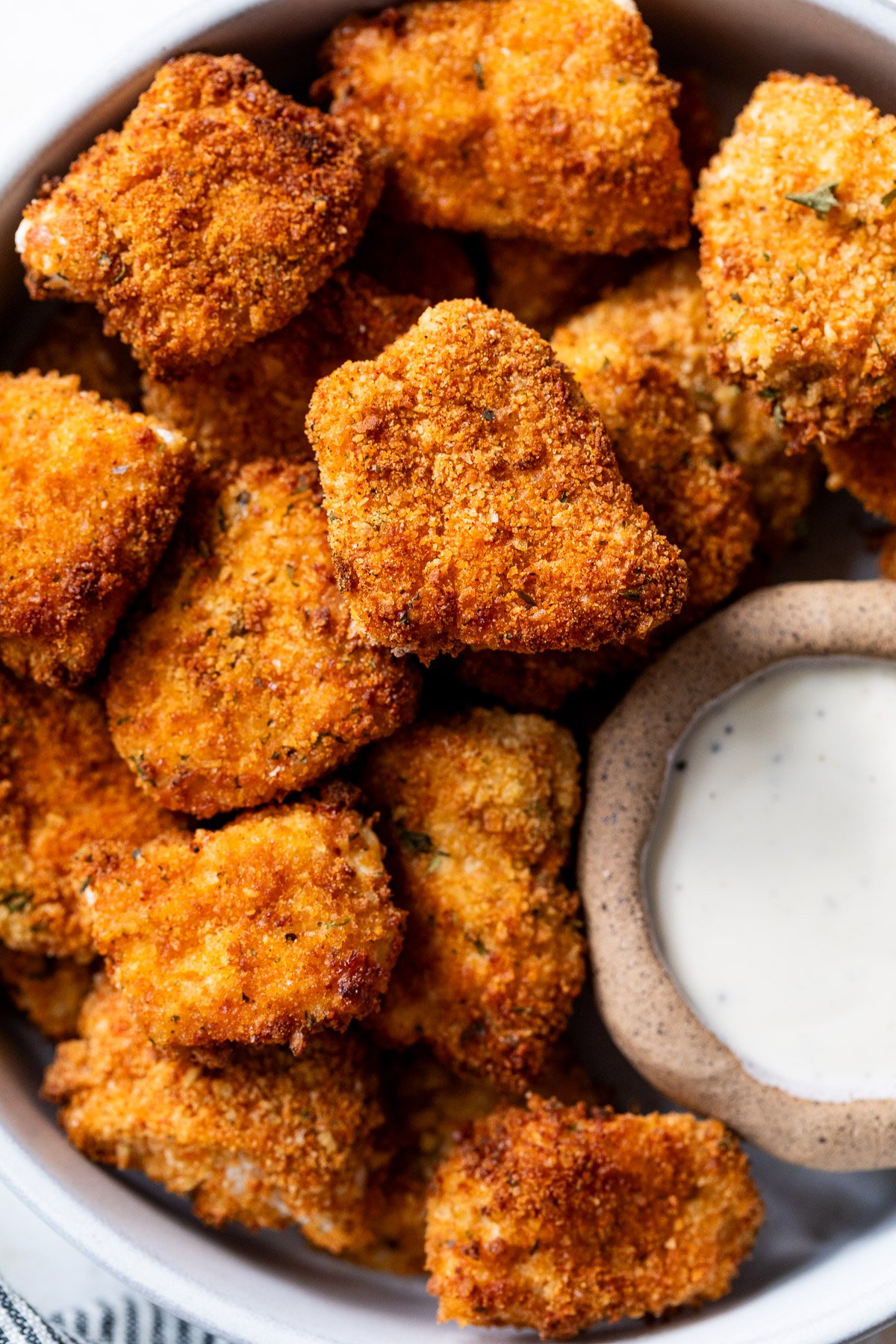 A bowl of crispy breaded air fryer chicken nuggets with a side of creamy white dipping sauce.