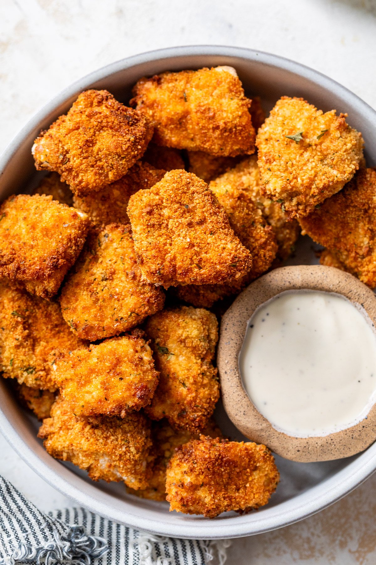 A bowl of crispy, golden-brown air fryer chicken nuggets with a side of creamy dipping sauce.