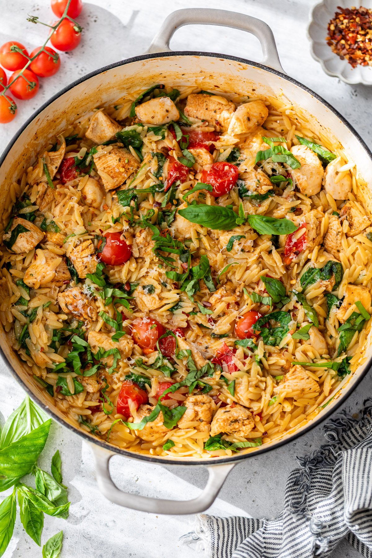 A pan of creamy orzo and chicken, tomatoes, fresh basil, and spinach, garnished with herbs.