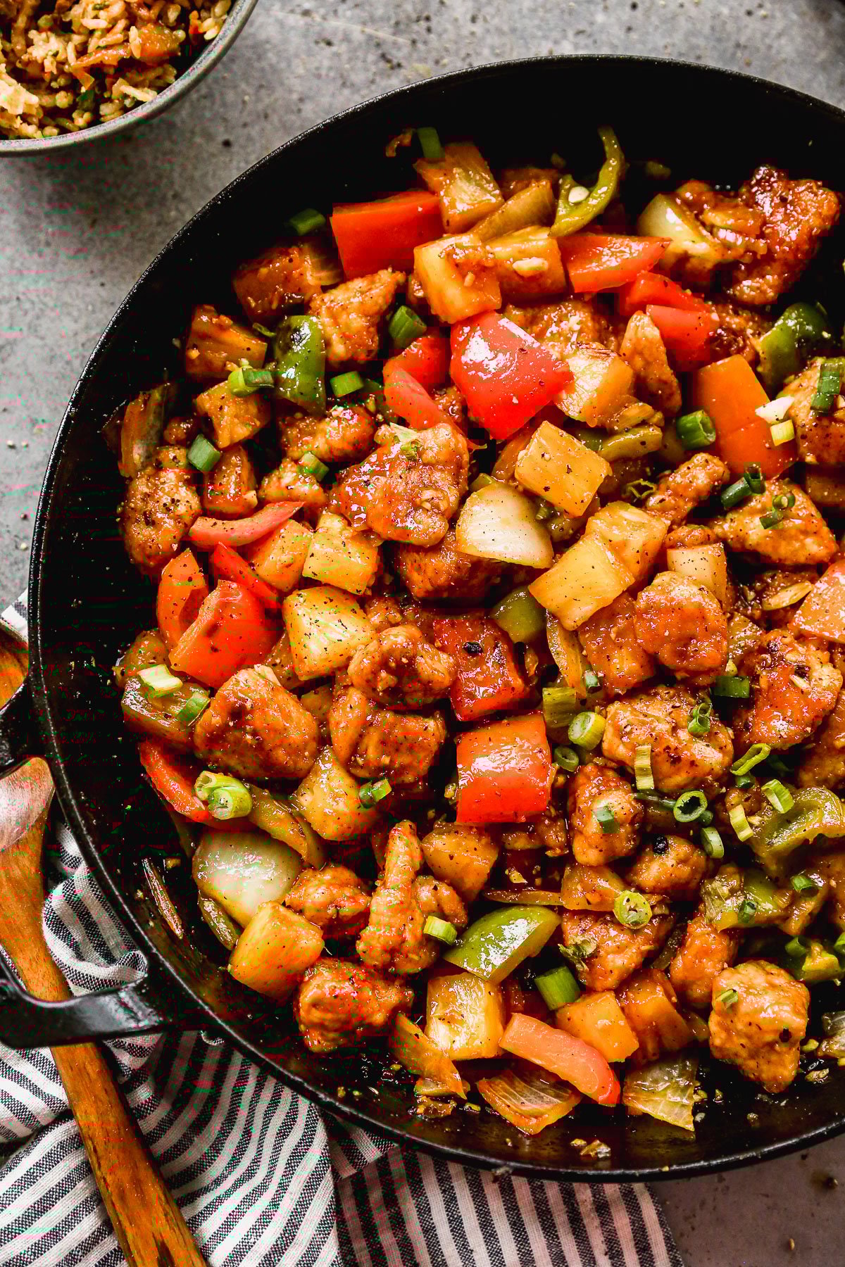 A skillet filled with stir-fried sweet and sour pork, bell peppers, onions, pineapple, and green onions.