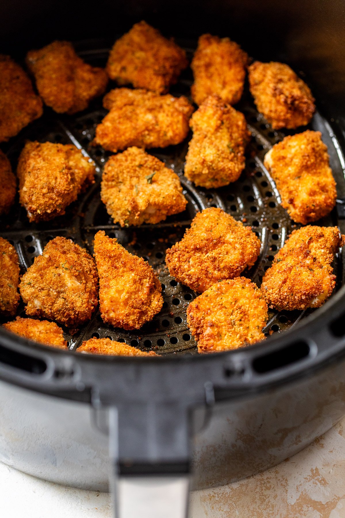 Breaded chicken nuggets cooking in an air fryer basket, golden brown and crispy.