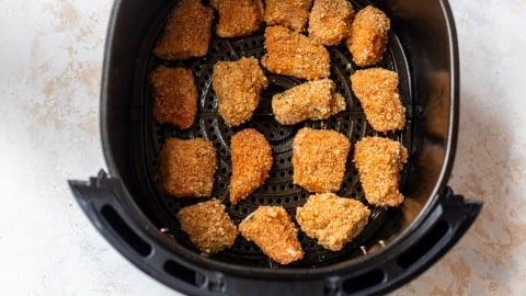 Breaded chicken nuggets arranged in a single layer inside an air fryer basket, ready for cooking.