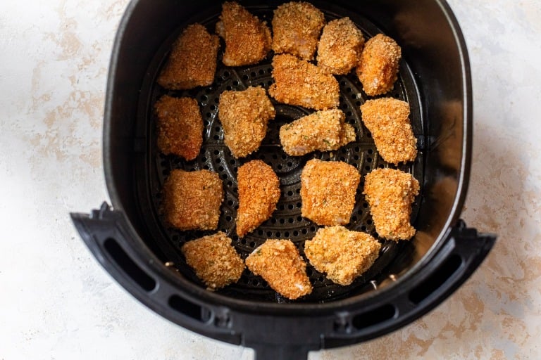 Breaded chicken nuggets arranged in a single layer inside an air fryer basket, ready for cooking.