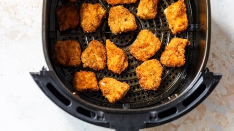 Breaded chicken nuggets arranged in a single layer inside an air fryer basket, ready to be cooked.