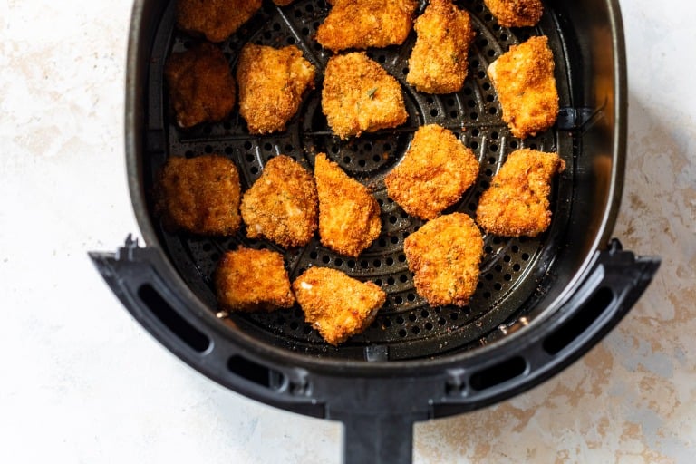 Breaded chicken nuggets arranged in a single layer inside an air fryer basket, ready to be cooked.