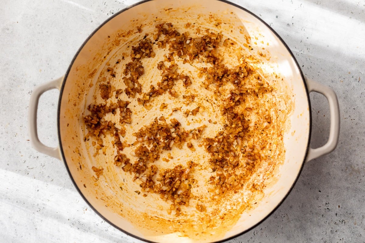 Diced shallots sautéed with spices in a large white pot on a light-colored surface.