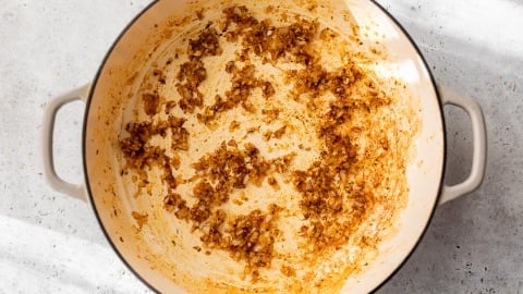 Diced shallots sautéed with spices in a large white pot on a light-colored surface.
