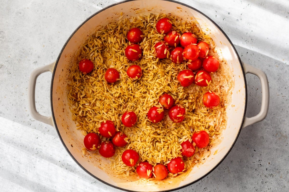 Orzo pasta and cherry tomatoes cooking in a large white pot on a light gray countertop.