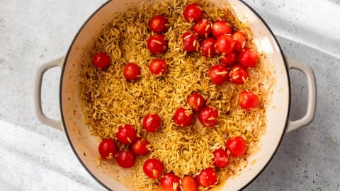 Orzo pasta and cherry tomatoes cooking in a large white pot on a light gray countertop.