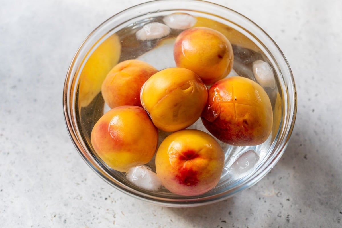 A bowl of yellow and red peaches sits in ice water, with a few ice cubes floating around them.