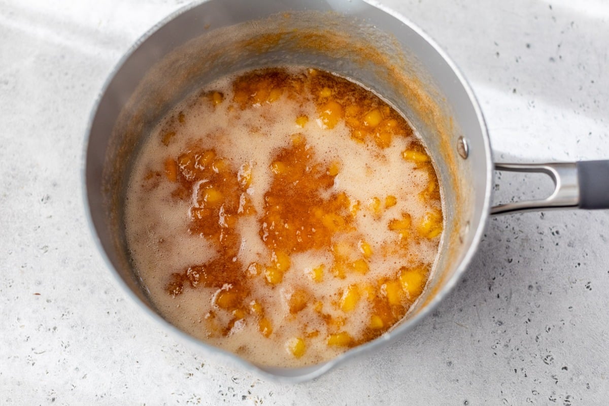 A saucepan filled with bubbling peach jam on a light countertop.