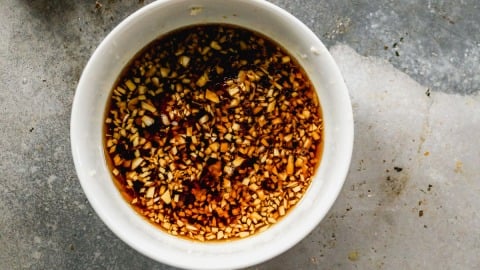 White bowl filled with sweet and sour sauce sits on a grey, textured surface.