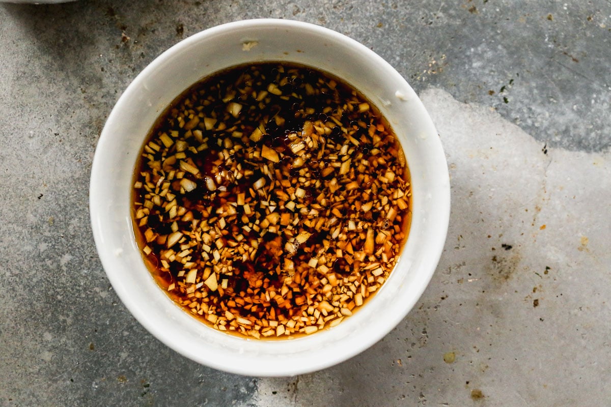 White bowl filled with sweet and sour sauce sits on a grey, textured surface.