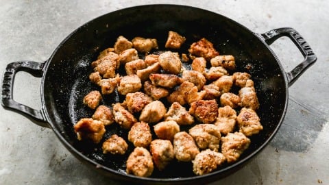 Cast iron skillet with browned, crispy pork pieces on a gray countertop.