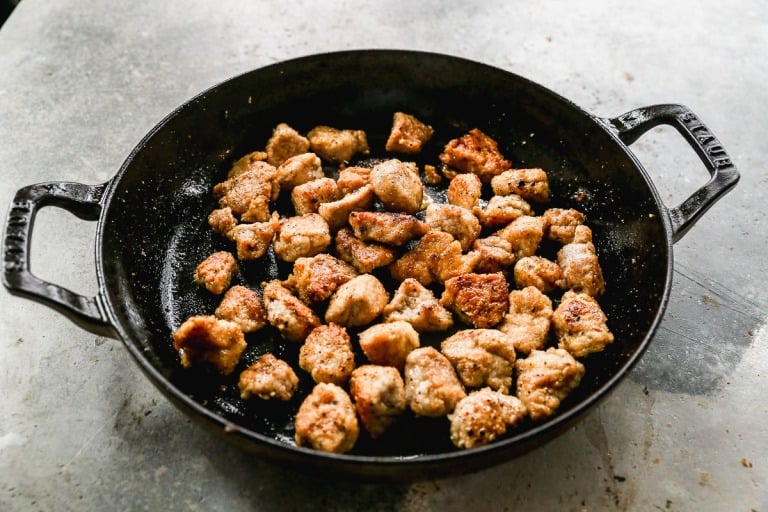 Cast iron skillet with browned, crispy pork pieces on a gray countertop.