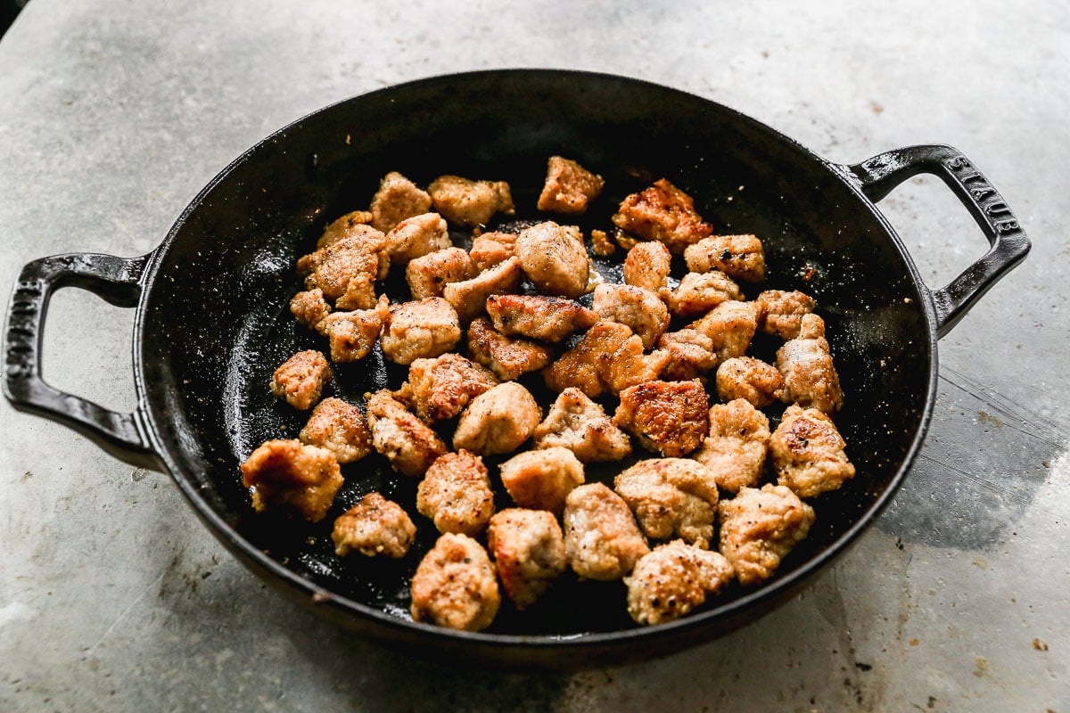 Cast iron skillet with browned, crispy pork pieces on a gray countertop.