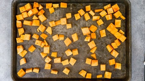 Cubed roasted butternut squash spread out on a baking sheet, ready to be roasted.
