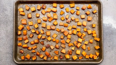 Baking sheet with evenly spaced, roasted butternut squash cubes on a gray countertop.