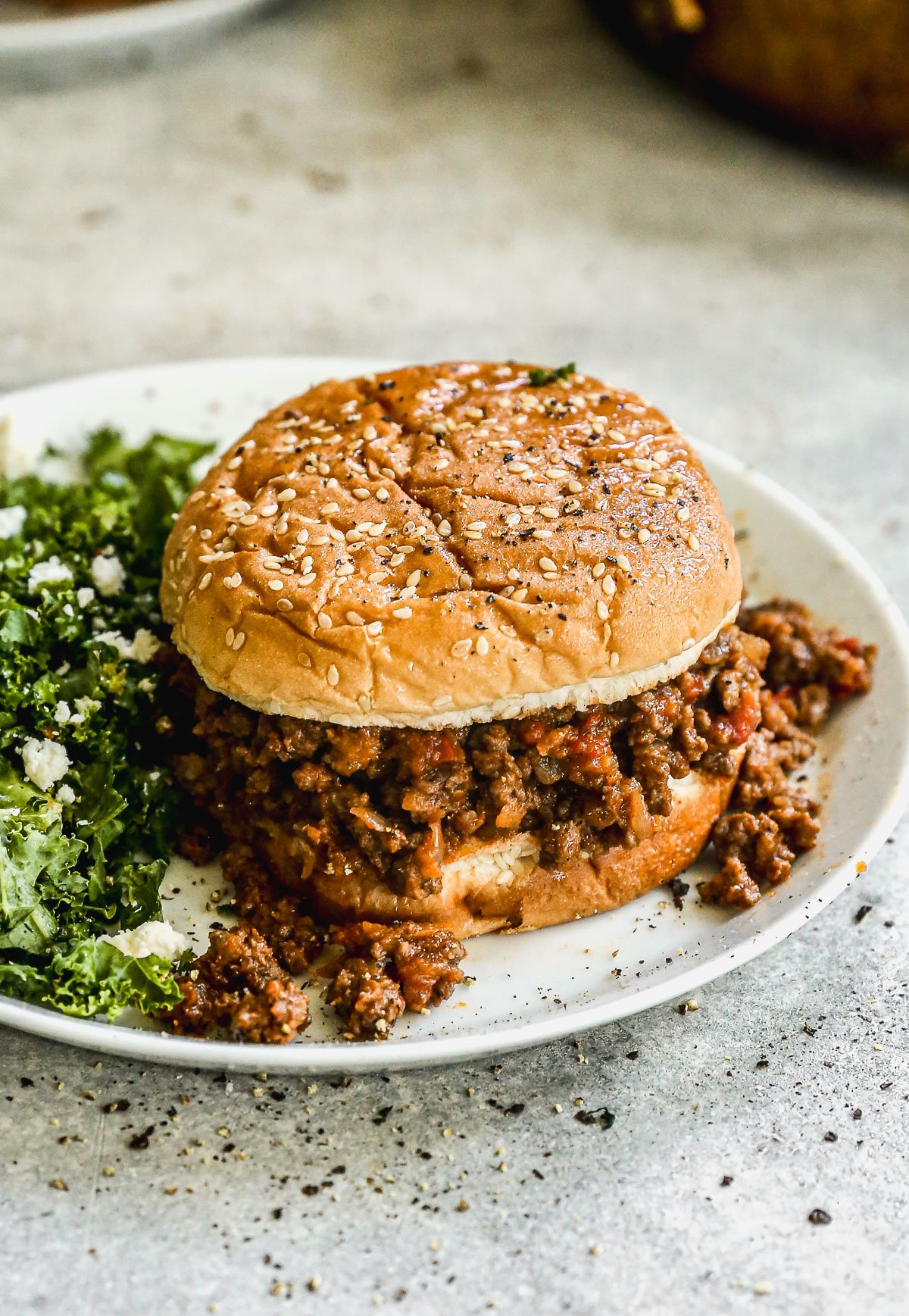 A sloppy joe sandwich on a plate with a side of leafy green salad topped with crumbled cheese.