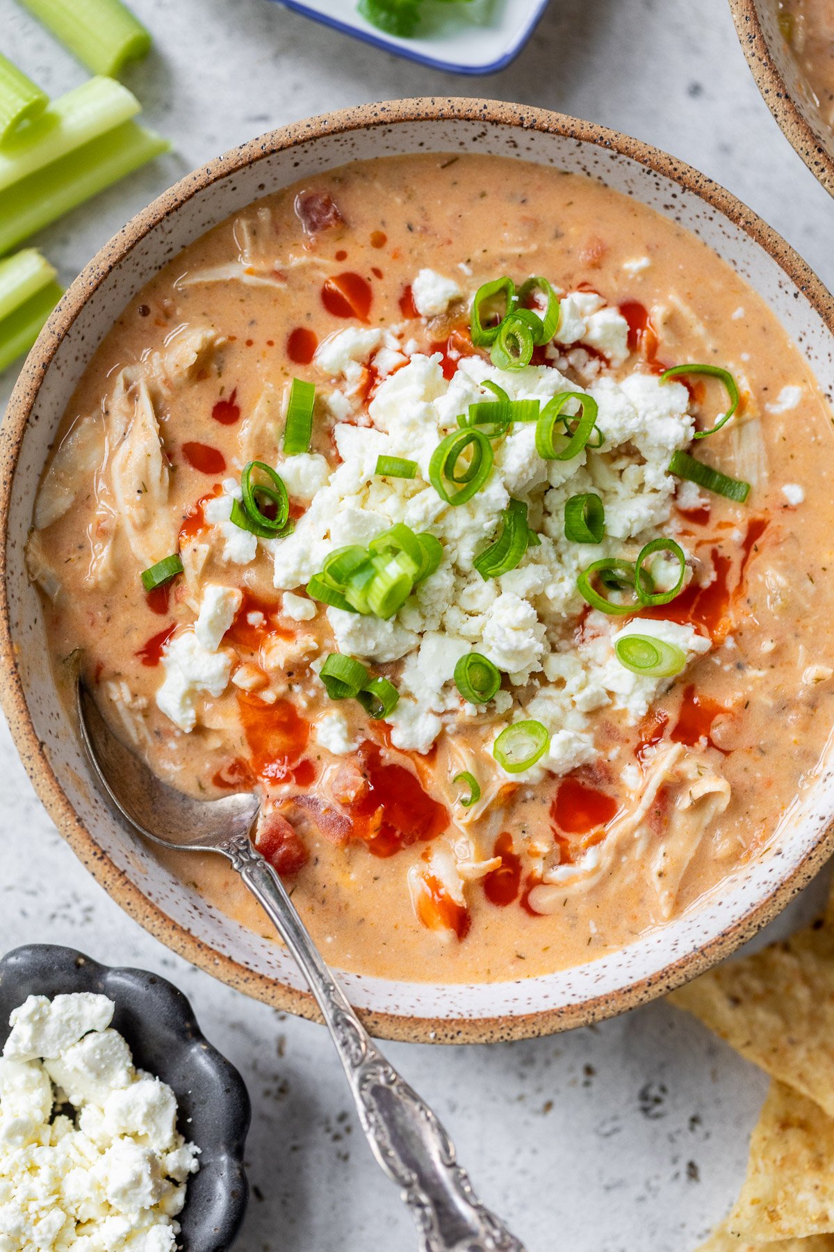 A bowl of creamy Buffalo chicken chili topped with crumbled cheese, chopped green onions, and a drizzle of hot sauce.