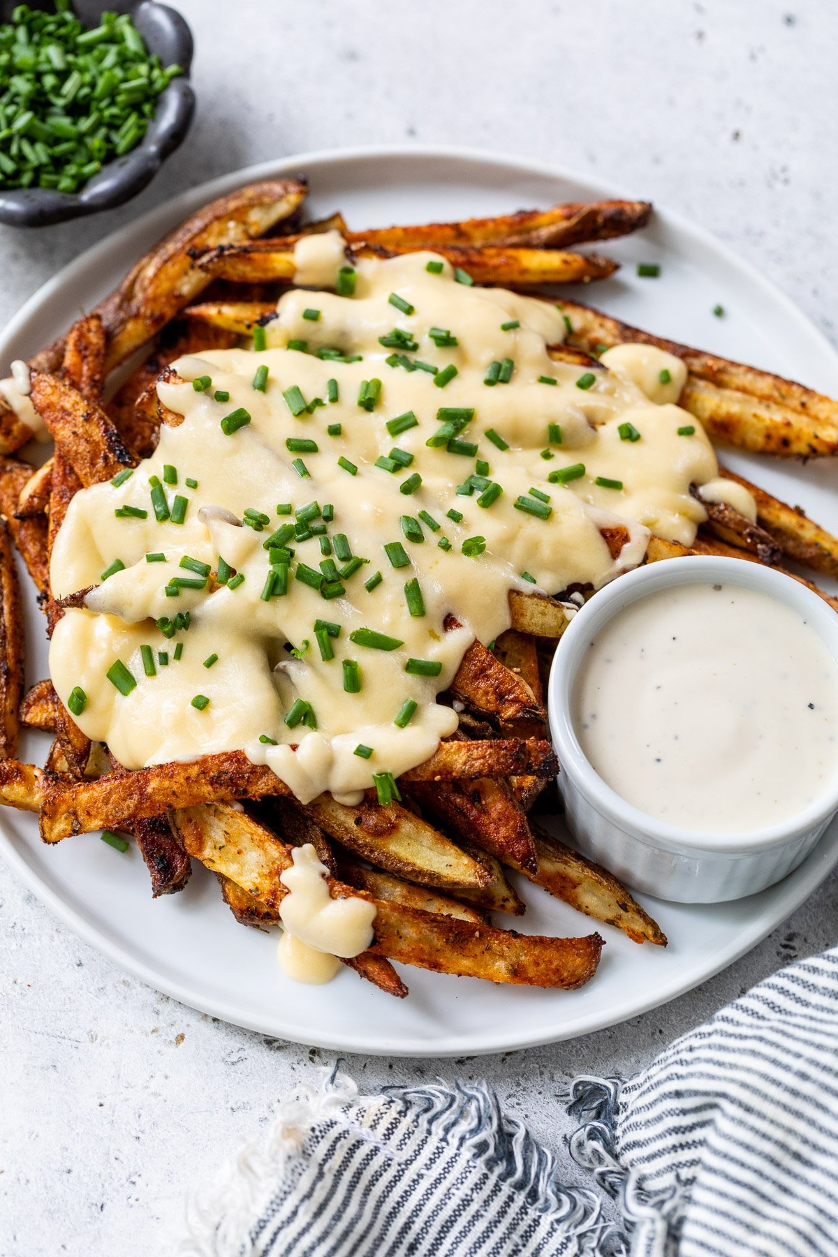 Plate of voodoo fries topped with melted cheese and chopped chives, served with a cup of creamy dipping sauce.