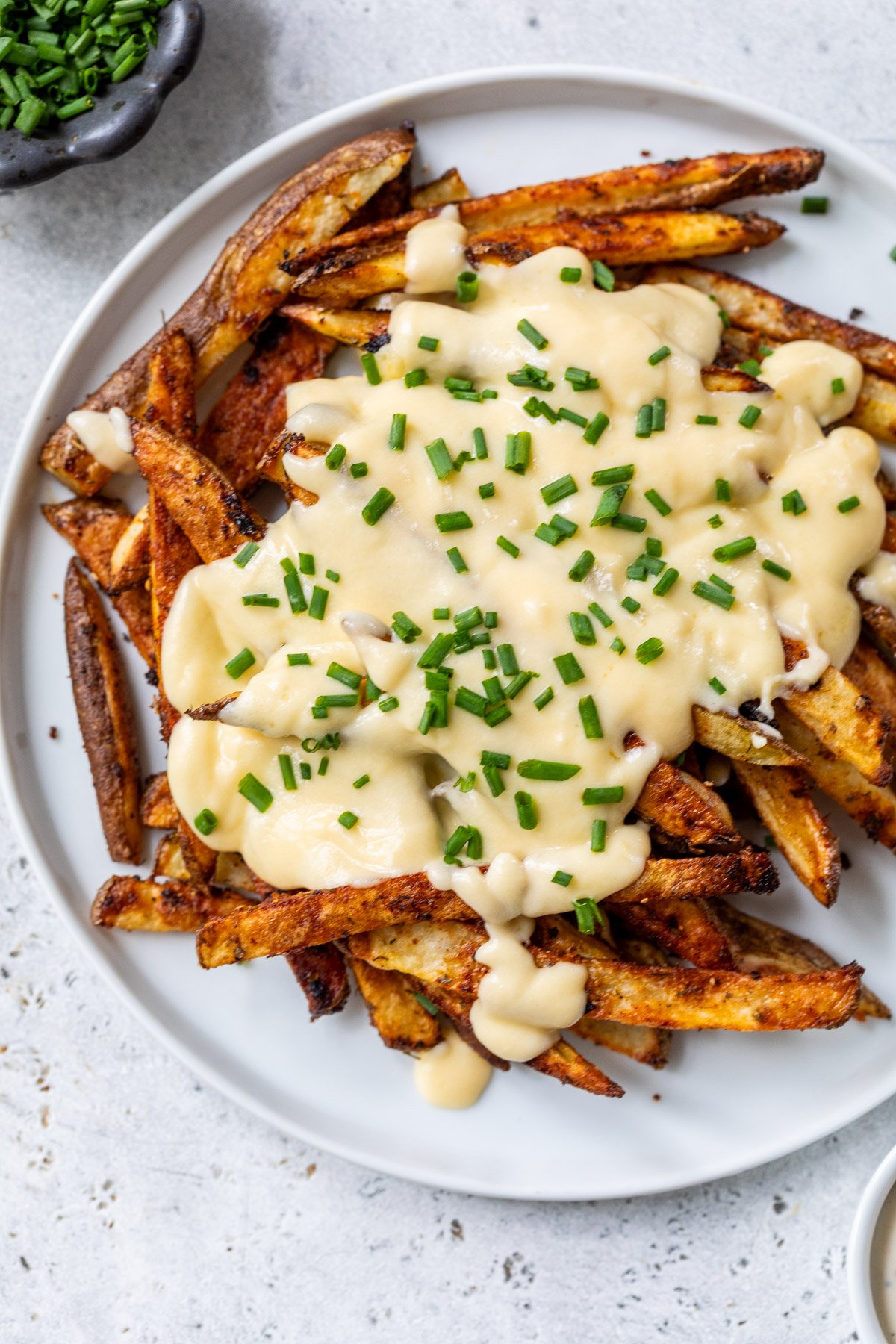 A plate of crispy voodoo fries topped with cheese sauce and chopped chives on a light-colored table.