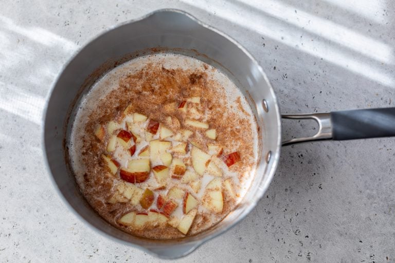 A saucepan with chopped apples, cinnamon, and oatmeal simmering on a light-colored countertop.