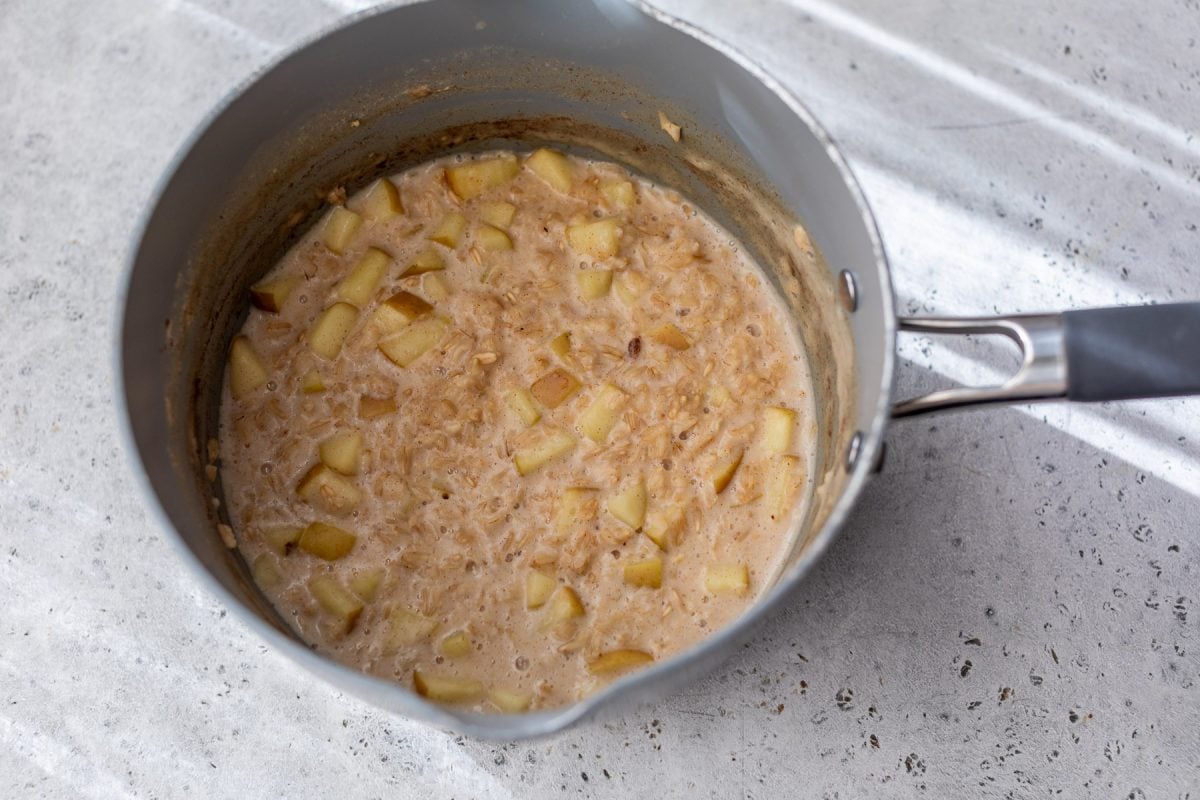 A saucepan filled with oatmeal and diced apples on a light-colored countertop.