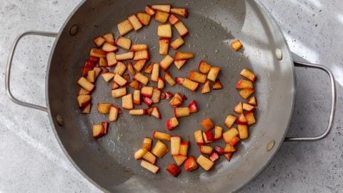 Diced apples sautéing in a large gray skillet on a light-colored countertop.