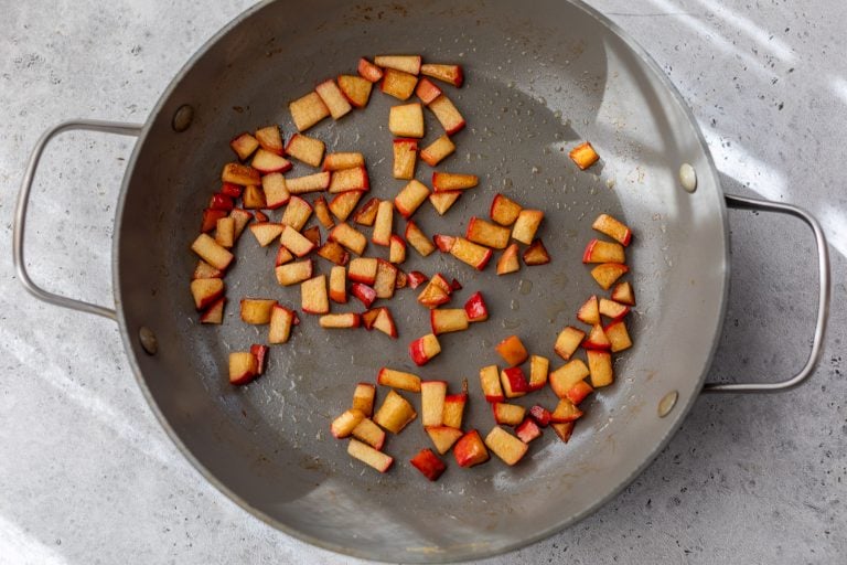 Diced apples sautéing in a large gray skillet on a light-colored countertop.