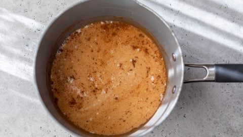 A saucepan containing ingredients for apple cinnamon oatmeal with specks of cinnamon on a light gray countertop.